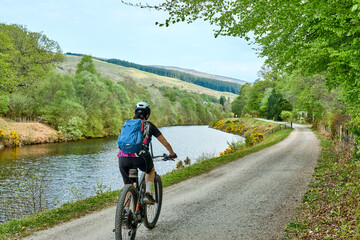 active senior woman riding her electric mountain bike along the Caledonian Canal near Fort William...
