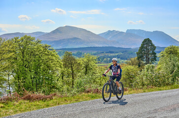 Fototapeta premium active senior woman riding her electric mountain bike above the Caledonian Canal near Fort William in Scotland with Ben Nevis summit in background, UK