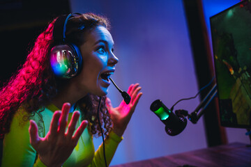 Young female gamer actively engaged in streaming video games under dynamic neon lighting during an...