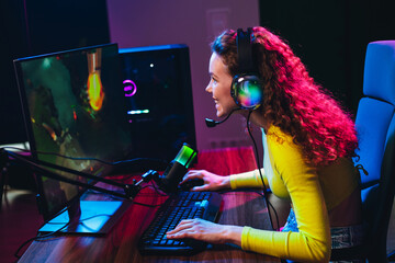 Young female gamer enjoying exciting video games at home with neon lights and professional...