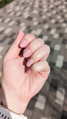 Manicured hand showing shiny pink nail polish against patterned background