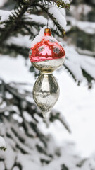 Red and white glass Christmas ornament hanging on snow-covered pine tree during winter season