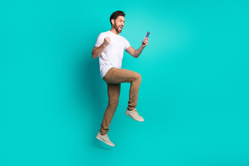 Excited young man celebrates success while holding a smartphone against a vibrant teal background