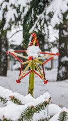 Decorative Christmas star, red and gold, covered in snow, amidst evergreen trees