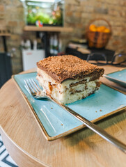 Delicious tiramisu dessert on blue plate, close view with fork on wooden table