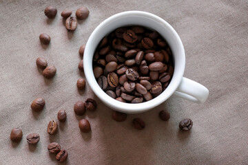 Coffee cup and roasted coffee beans on brown fabric.