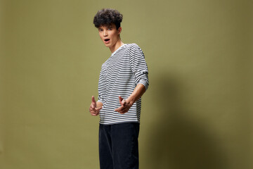 young man in striped shirt posing confidently against green background with curly hair and casual...