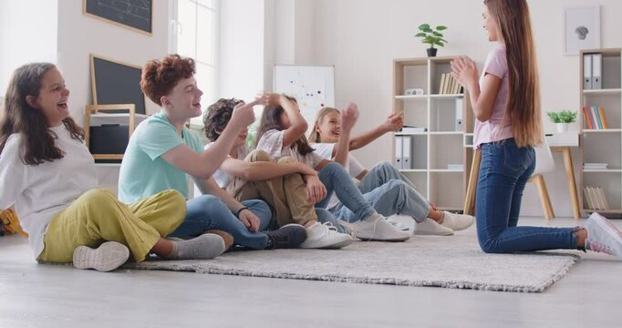 Cheerful happy children playing game, boy, girl friends sitting on floor carpet in class room to have fun laughing together with classmates, enjoy free time after lesson playing, talking activity