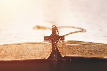  A crucifix necklace placed vertically in the middle of an open Bible, symbolizing Christian faith,...