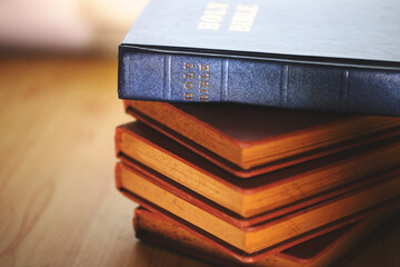 Stack of vintage Bibles with a close-up focus on the spine of a blue Holy Bible on top. Represents...