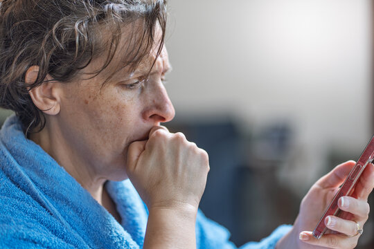 A woman is looking at her phone while wearing a blue robe. She is in a contemplative mood