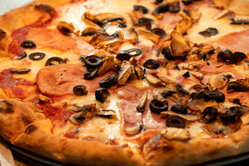 Close-up photo of a delicious pizza topped with melted cheese, slices of meat, and green olives....
