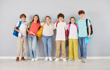 Group portrait of happy school children in colorful clothes standing together in row and hugging...