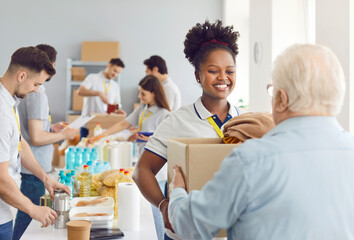 Happy smiling african american volunteer working at charity center giving free food donations for mature man in charitable foundation. Humanitarian aid, volunteering and social help for poor concept.