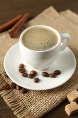 Aromatic coffee in cup, beans, brown sugar and cinnamon on table, closeup