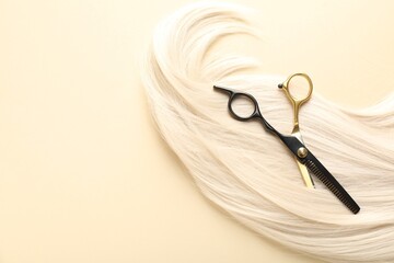 Hair lock and scissors on beige background, top view. Space for text