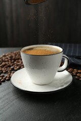 Adding cinnamon to aromatic coffee at black table, closeup