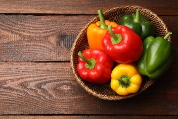 Fresh colorful bell peppers in wicker basket on wooden table, top view. Space for text
