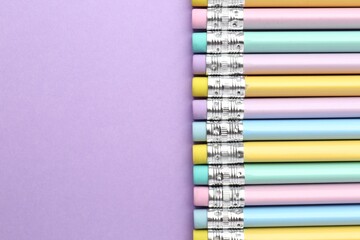 Many graphite pencils with erasers on violet background, flat lay. Space for text