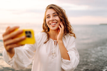 Portrait of young woman with phone in hands takes selfie with the sea in background. Beautiful...