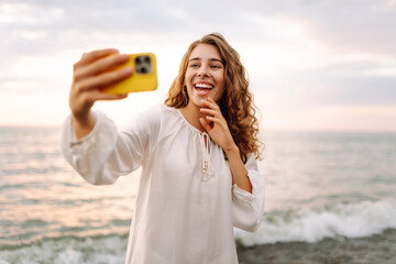 Portrait of young woman with phone in hands takes selfie with the sea in background. Beautiful...
