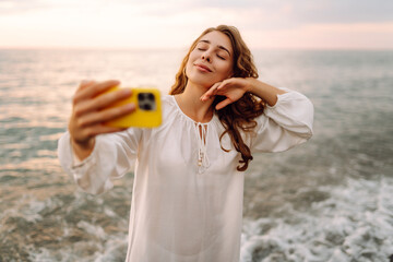 Portrait of young woman with phone in hands takes selfie with the sea in background. Beautiful...
