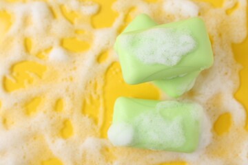 Soap bars with foam on yellow background, flat lay. Space for text