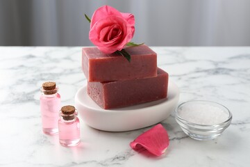 Soap bars, cosmetic products and beautiful rose on white marble table