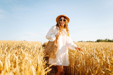 Young woman enjoying sunny day walking in golden wheat field. Beautiful woman in white dress and...