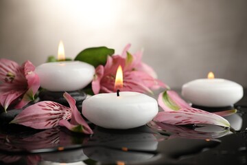 Burning candles and beautiful flowers on wet black table, closeup. Space for text