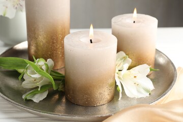 Burning candles and beautiful flowers on white table, closeup