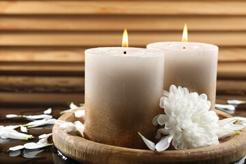 Burning candles and beautiful flowers on wet black mirror surface, closeup