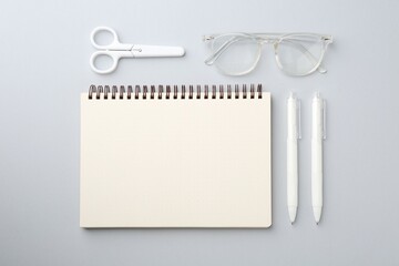 Notebook, scissors, pens and glasses on gray background, flat lay
