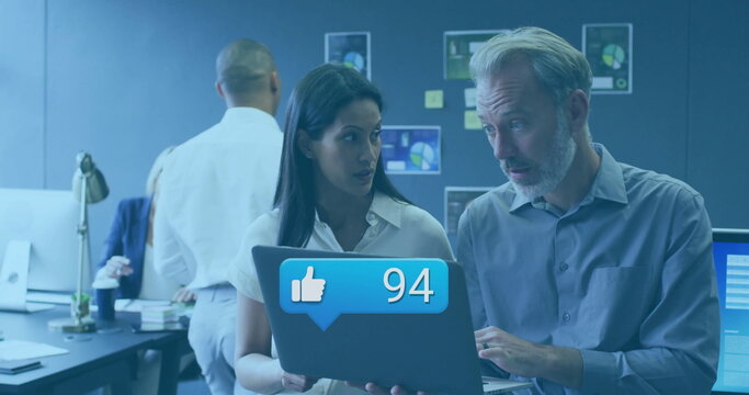 Reviewing laptop notification, woman and man collaborating in office, with desk lamp coffee charts