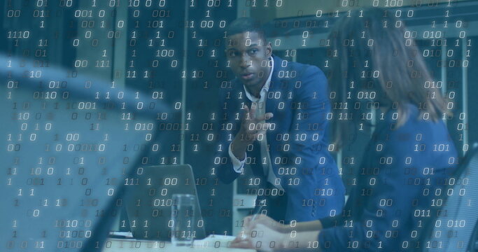 Gesturing businessman in dark blue suit leaning on conference table at office, with laptop and code - Powered by Adobe