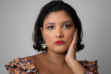 Sad woman with hand on face, looking at camera. Horizontal studio portrait ideal for skin conditions, mental health issues, femininity and self-esteem problems. Copy space on gray background.
