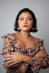 Confident and empowered woman wearing floral pattern dress, with arms crossed. Ideal for beauty, female empowerment, fashion and femininity. Studio portrait with copy space on light gray background.