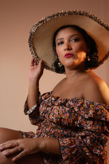Vertical portrait of beautiful elegant woman wearing a straw hat and floral pattern dress. Ideal for vacations, beauty, summer, sunset light, lifestyle. Studio shot with copy space.