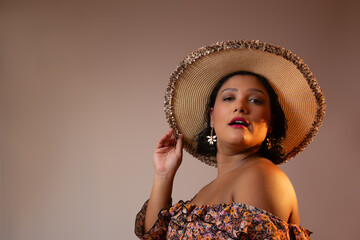 Sensual woman with brown skin, wearing a straw hat, looking at camera. Perfect for vacations, beauty, summer, luxury lifestyle, self-love. Horizontal studio portrait with copy space.