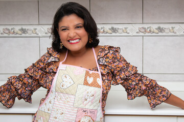 Beautiful happy woman with open arms, wearing apron in home kitchen. Cheerful housewife laughing at camera. Ideal for cooking meals, home chef, gastronomy and lifestyle.