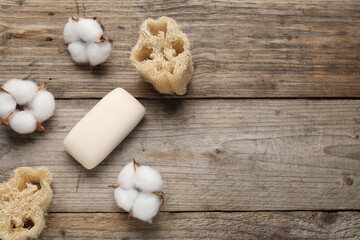 Soap bar, loofah sponges and cotton flowers on wooden table, flat lay. Space for text