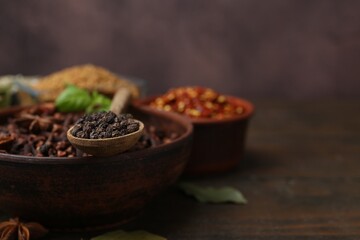Different aromatic spices on wooden table against brown background, closeup. Space for text
