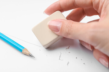 Woman using eraser at white paper, closeup
