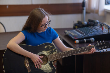 Young woman playing guitar in recording studio. 