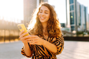 A close-up of a yellow phone held by a young woman against the backdrop of an urban metropolis. A...