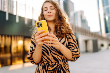 A close-up of a yellow phone held by a young woman against the backdrop of an urban metropolis. A...