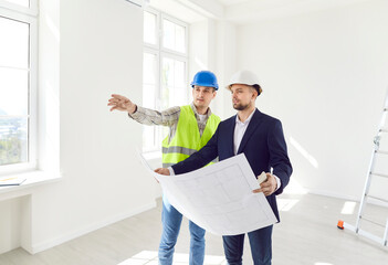 Two men in helmets with a drawing of the building inspect the empty room. The foreman shows the work done according to the plan. The contractor checks the work. Concept construction