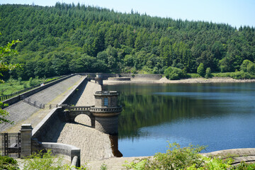 Derbyshire, England - June 20 2025: Scenic view of a dam and reservoir with intricate stone structure, surrounded by lush green hills.