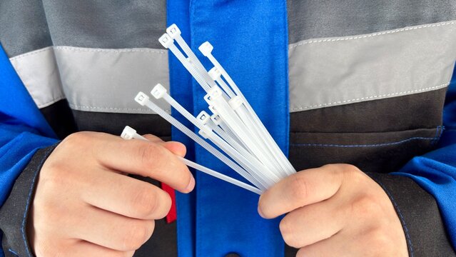 Closeup of hands holding several white cable ties, with a person wearing a blue jacket in the background
