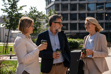 Diverse business people having coffee and water break outdoors, pleasant conversation in urban...